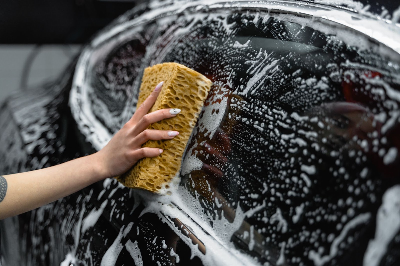 Hand washing a soapy black car window with a sponge